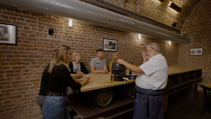 Ein Köbes steht an einem Tisch und erklärt fünf weiteren Teilnehmern das Bier-Zapfen